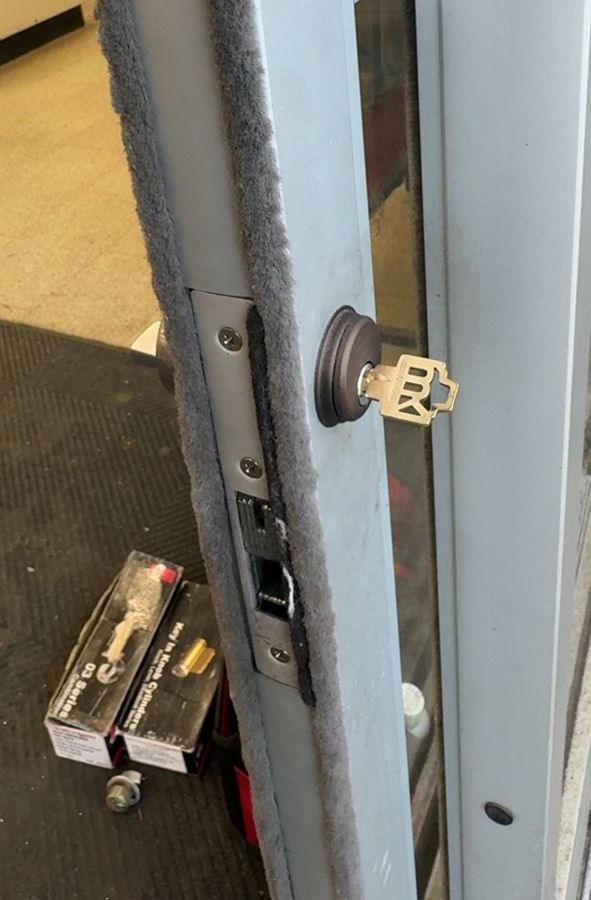 Key side of the same storefront door after the repair, new parts boxes on the mat, Kannapolis NC